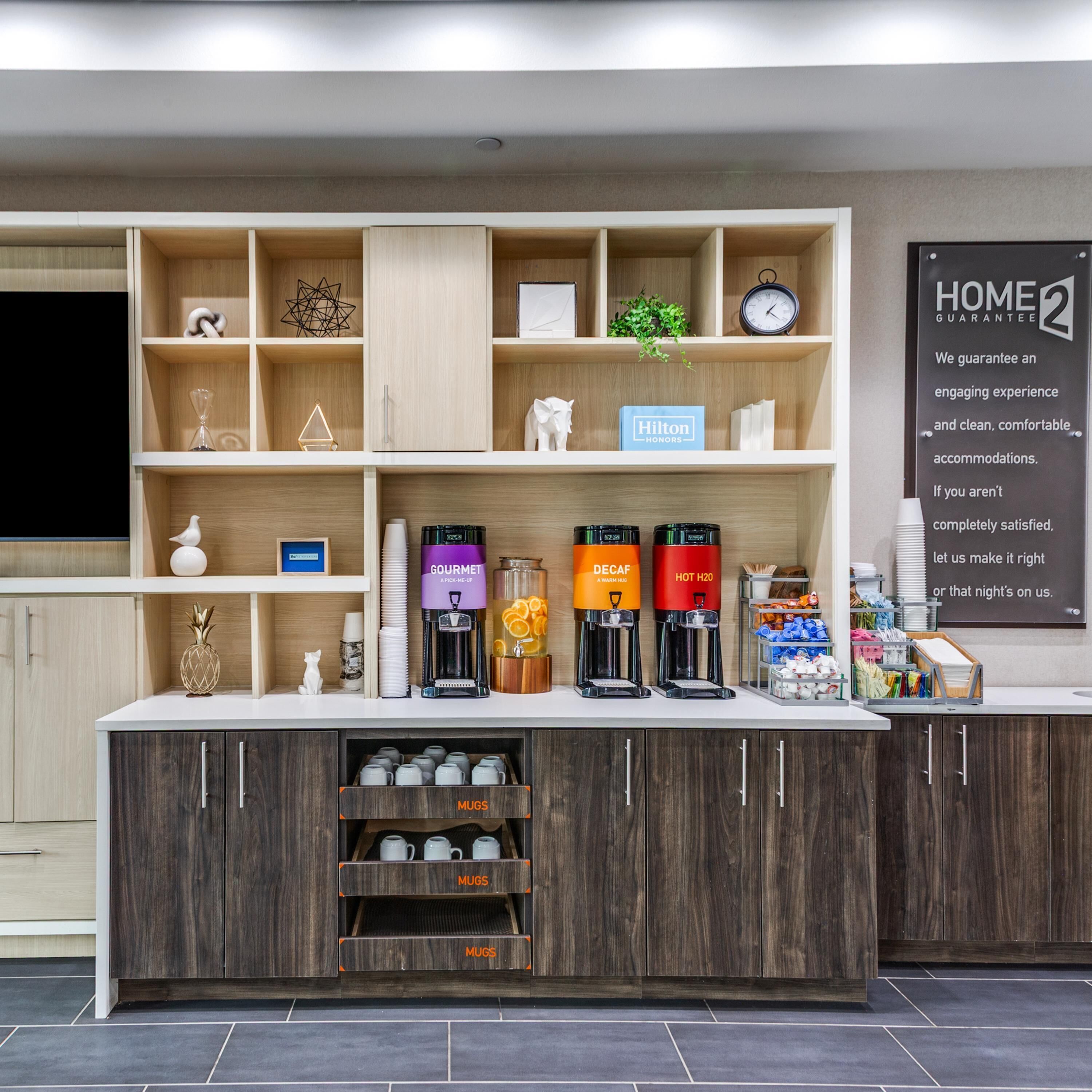 Uma área de recepção de hotel com um espaço para café, um relógio e um aviso que diz 'HOME GUARANTEE'.