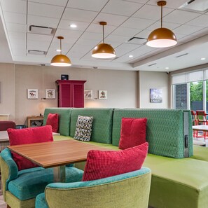 Een modern interieur met een groene bank, rode kussens, blauwgroene stoelen en hanglampen.