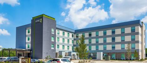 A modern hotel with a prominent "Home 2" sign, multiple floors, and a parking lot with several cars.