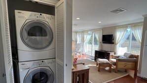 Un lavadero con lavadoras apiladas y una sala de estar con sofá, televisión y vistas al exterior.