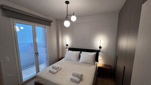 Un dormitorio moderno con una cama grande, dos lámparas de noche, una puerta corrediza de vidrio a un balcón y suelo de madera.