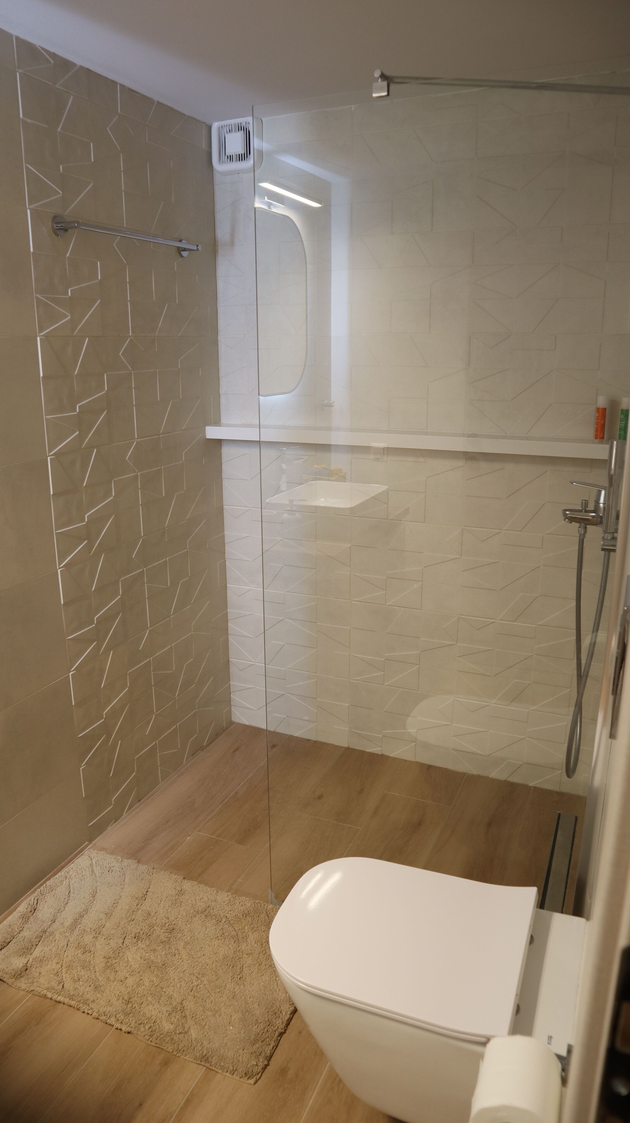 A modern bathroom with a glass shower enclosure, a white toilet, and a beige rug.
