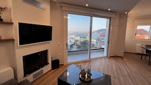 Una sala de estar moderna con un televisor de pantalla plana, una chimenea y un gran ventanal corredera que da a un balcón con vistas a la ciudad.