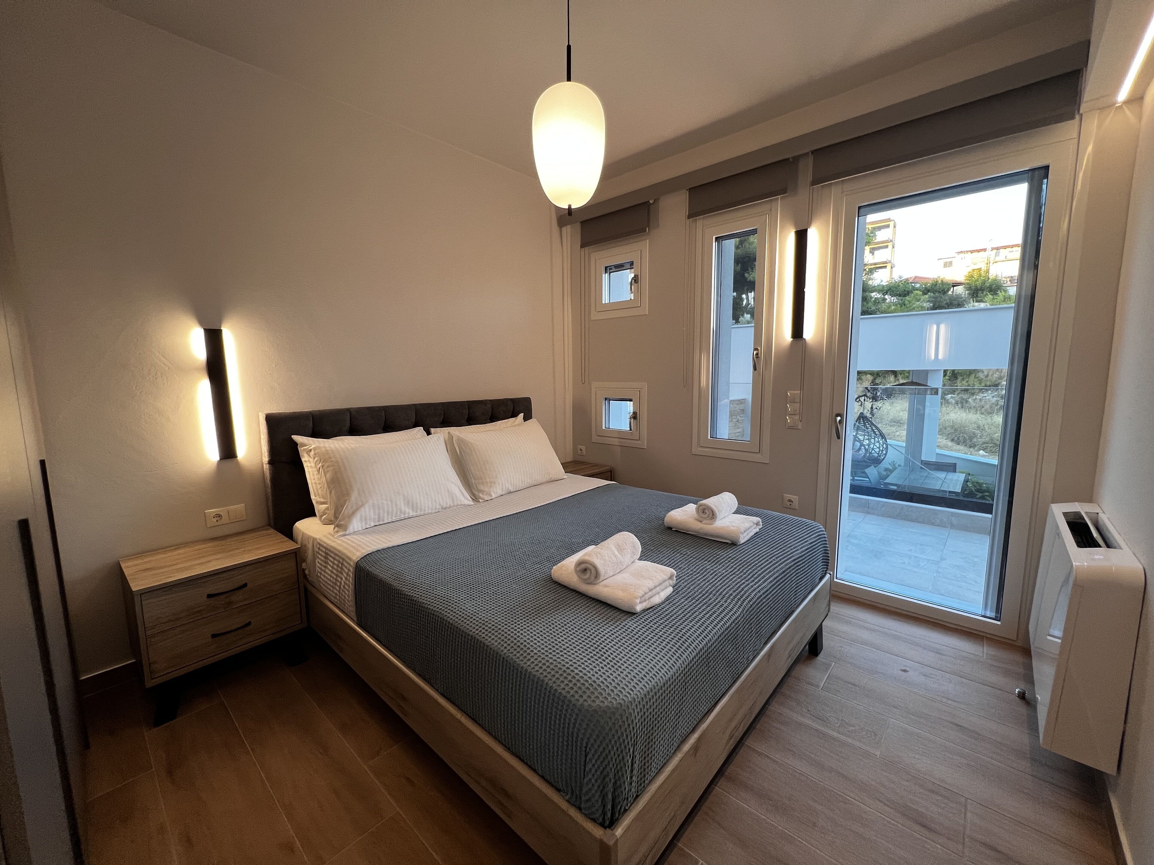 Una camera da letto moderna con un letto grande, comodini, una lampada a soffitto e una porta scorrevole in vetro che dà su un balcone.