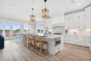 A modern kitchen with white cabinets, a large island, and pendant lighting. - OceanPearl- Private Heated Pool- 5 min walk to the beach! (Panama City Beach)