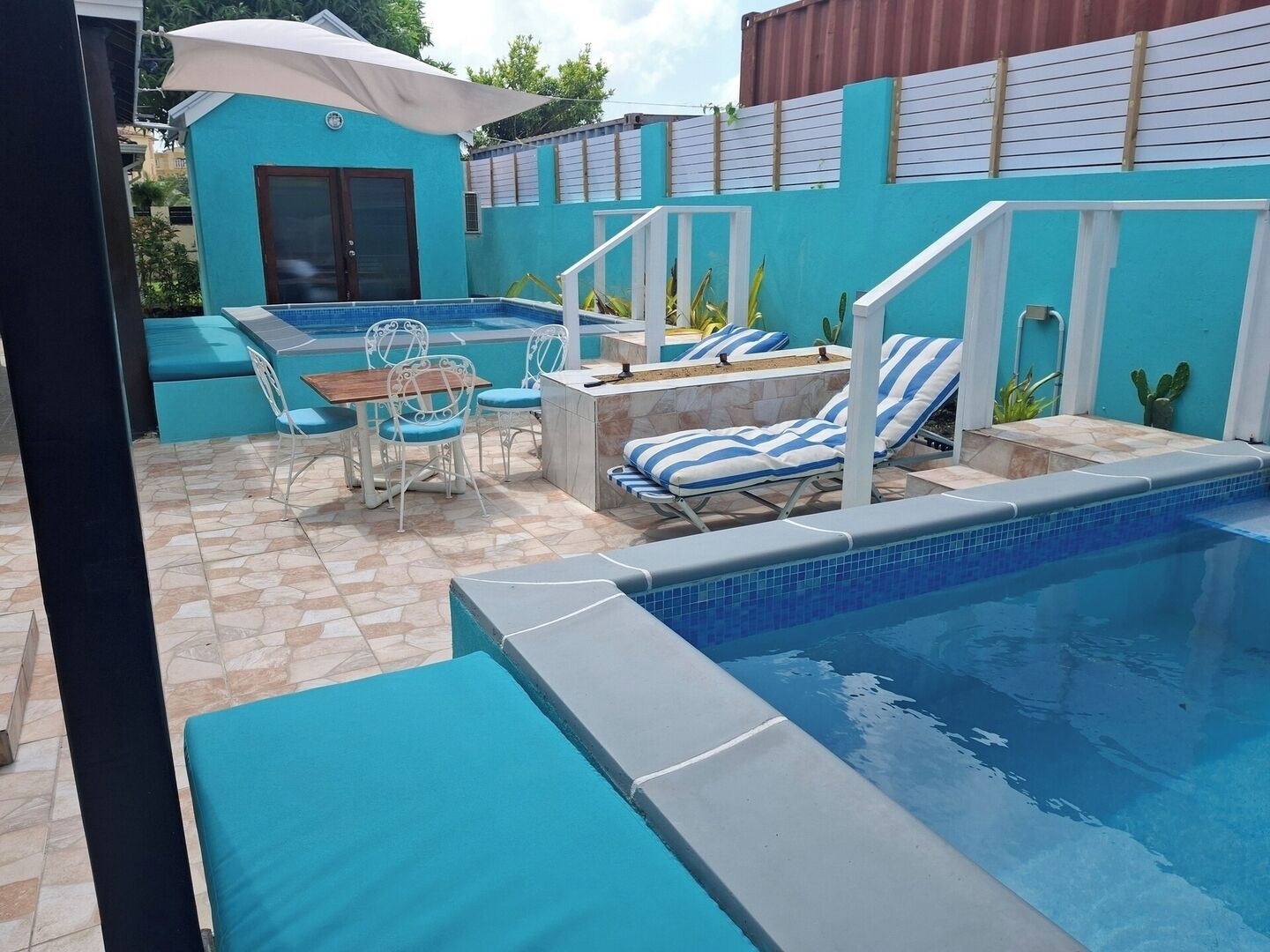 A swimming pool with lounge chairs and a table, surrounded by a tiled patio area.