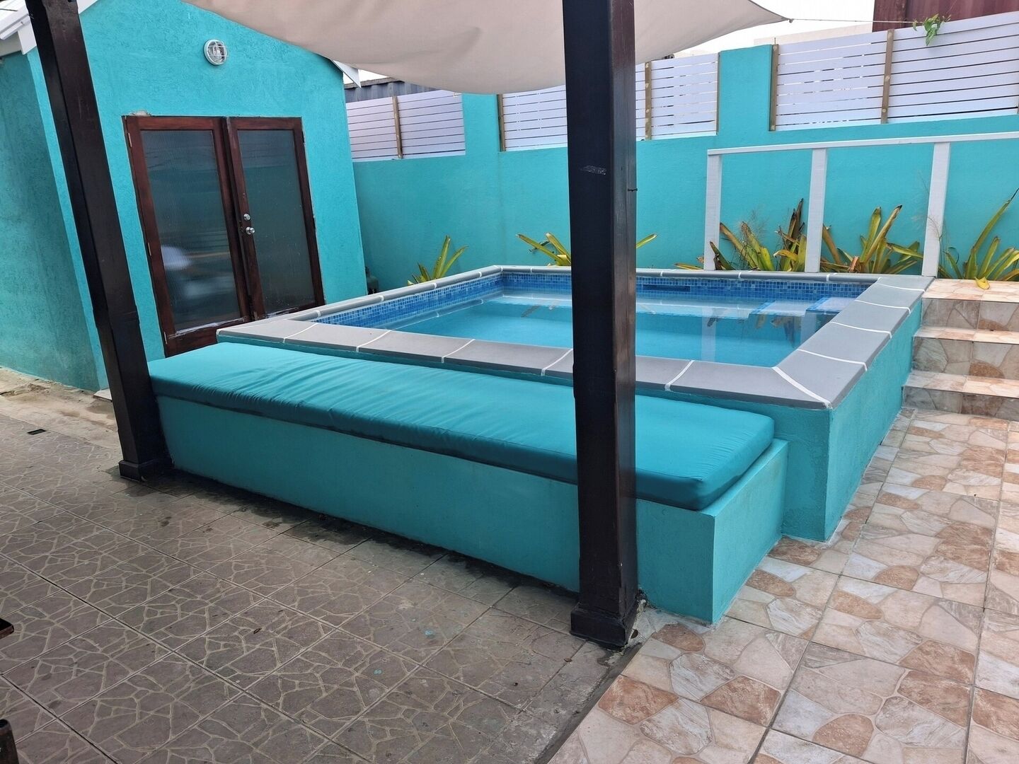 En swimmingpool med blå fliseterrasse og et overdækket opholdsområde.
