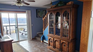 Ein geräumiges Wohnzimmer mit einem Holzkabinett, einem Deckenventilator und Blick durch eine Glastür auf eine Terrasse.
