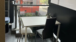 Ein Balkon mit Tisch und Stühlen, einer Whiteboard-Tafel und Blick auf ein mehrgeschossiges Gebäude mit Balkonen.