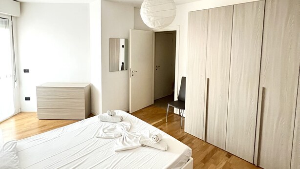 Ein modernes Schlafzimmer mit einem großen Bett, Holzboden, einem Kleiderschrank und einer Hängelampe.