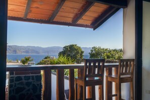 Ein Balkon mit Holzstühlen und einem Tisch, mit Blick auf eine malerische Berg- und Wasserlandschaft.