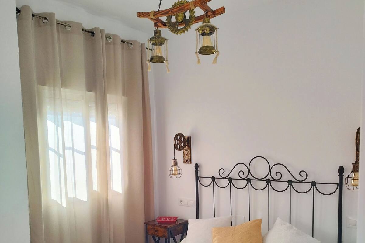 A neatly made bed with white and gold bedding, a wooden headboard, and a hanging light fixture above.