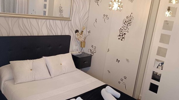 Ein ordentlich bezogenes Bett mit weißen Leinen, einem schwarzen Kopfteil und zwei zusammengerollten Handtüchern auf dem Bett.
