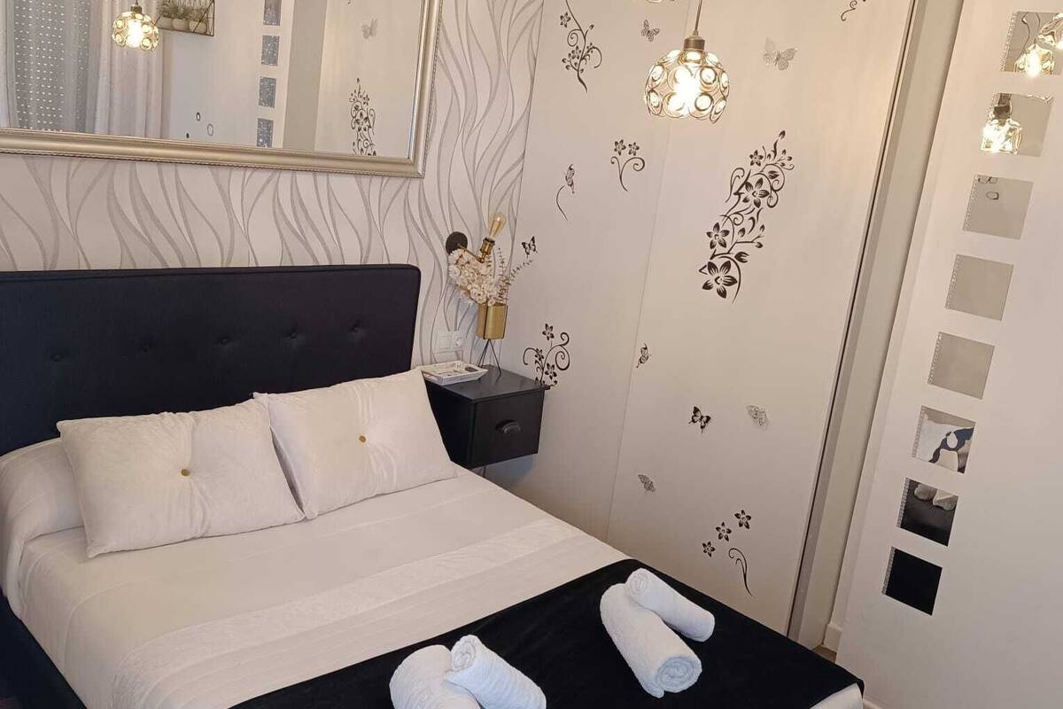 A neatly made bed with white linens, a black headboard, and two rolled towels on the bed.