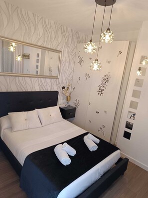 A neatly made bed with white linens, a black headboard, and two rolled towels on the bed. - Hostal Casa Blanca (Seville)