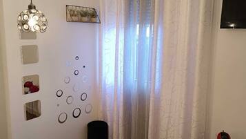 Ein Hotelzimmer mit einem Bett, zwei hängenden Pendelleuchten, einem an der Wand befestigten Fernseher, einem Fenster mit weißen Vorhängen und einem kleinen Tisch mit zwei Tassen.