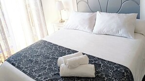 Ein ordentlich bezogenes Bett mit einem gemusterten Bettüberwurf, zwei Kissen und aufgerollten Handtüchern.