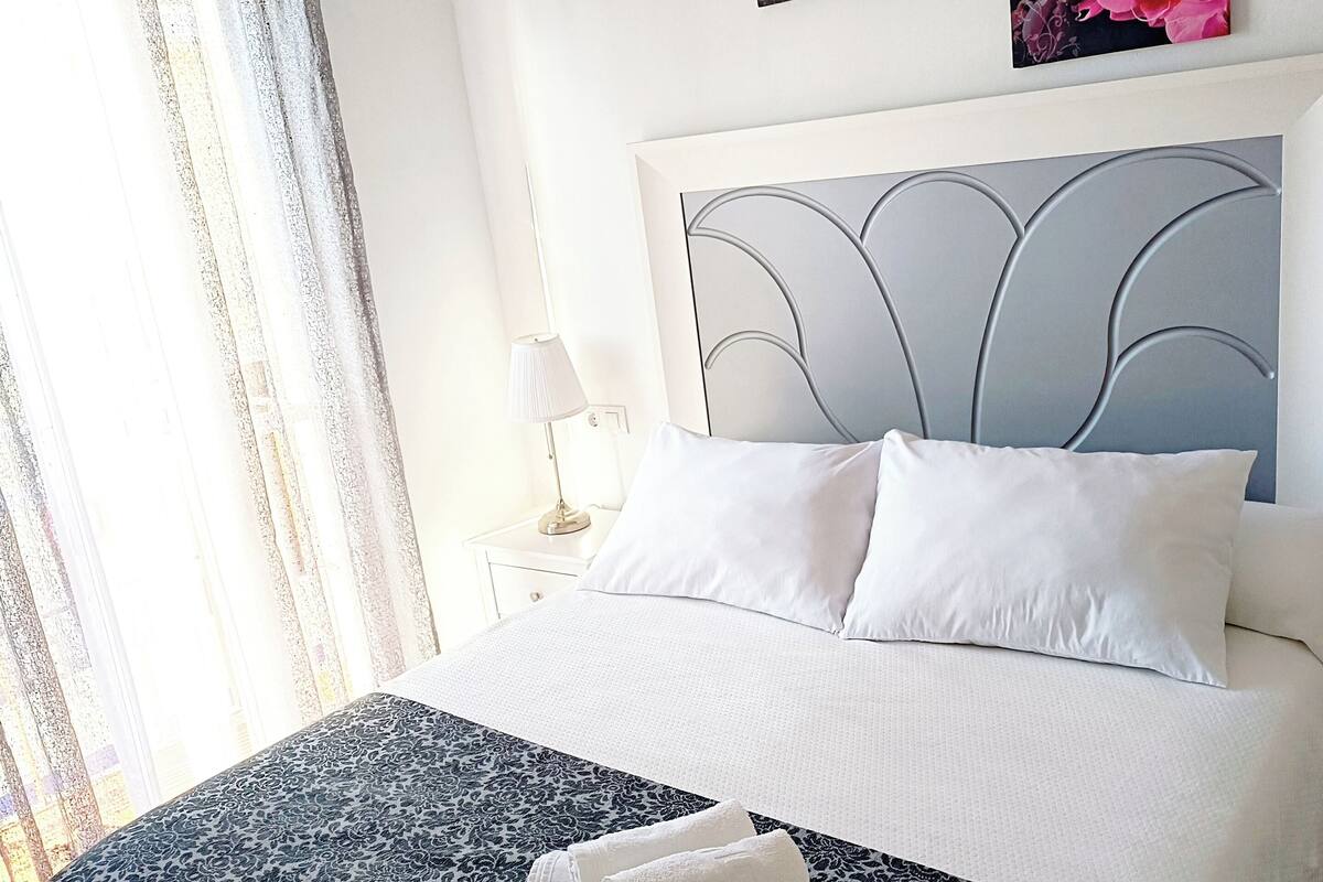 A neatly made bed with a patterned bedspread, two pillows, and rolled towels.