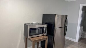 Eine Küche mit einer Mikrowelle auf einem Holztisch, einem schwarzen Kühlschrank und hellen Wänden.