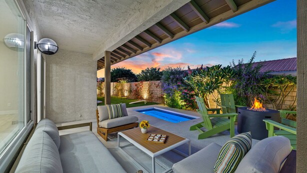 An outdoor patio with a pool, green chairs, a fire pit, and a sofa. - Lush Chic Living Private Backyard Heated Saltwater Pool (Indio)
