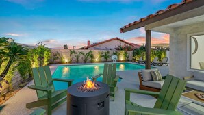 A backyard with a swimming pool, green chairs, a fire pit, and a patio area. - Lush Chic Living Private Backyard Heated Saltwater Pool (Indio)