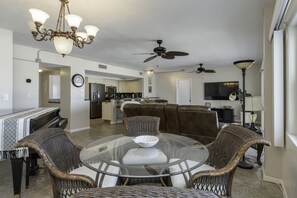 Uma sala de estar ampla com uma mesa de jantar de vidro cercada por cadeiras de vime, um sofá de couro marrom e um ventilador de teto.