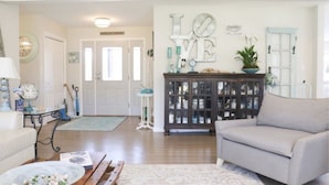 A spacious living room with a light-colored sofa, a wooden coffee table, and a decorative cabinet. A large wall decoration with the word "LOVE" is visible.