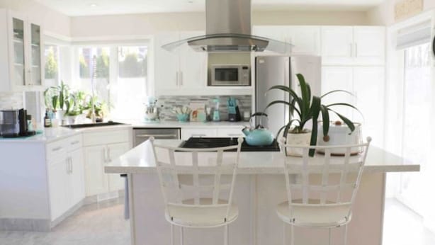 A modern kitchen with white cabinetry, a central island with chairs, a microwave, and a kettle.