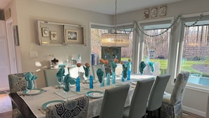 A dining room with a table set for six, featuring patterned tablecloths and blue glassware.