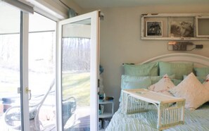 A bedroom with a bed, a nightstand, and a window with a view of the outdoors.