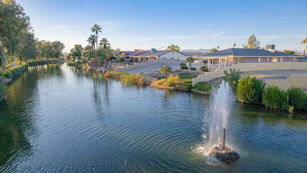 A serene lakeside scene with a fountain, surrounded by residential buildings and lush greenery. - Well-appointed home just steps from the Colorado river! (Needles)