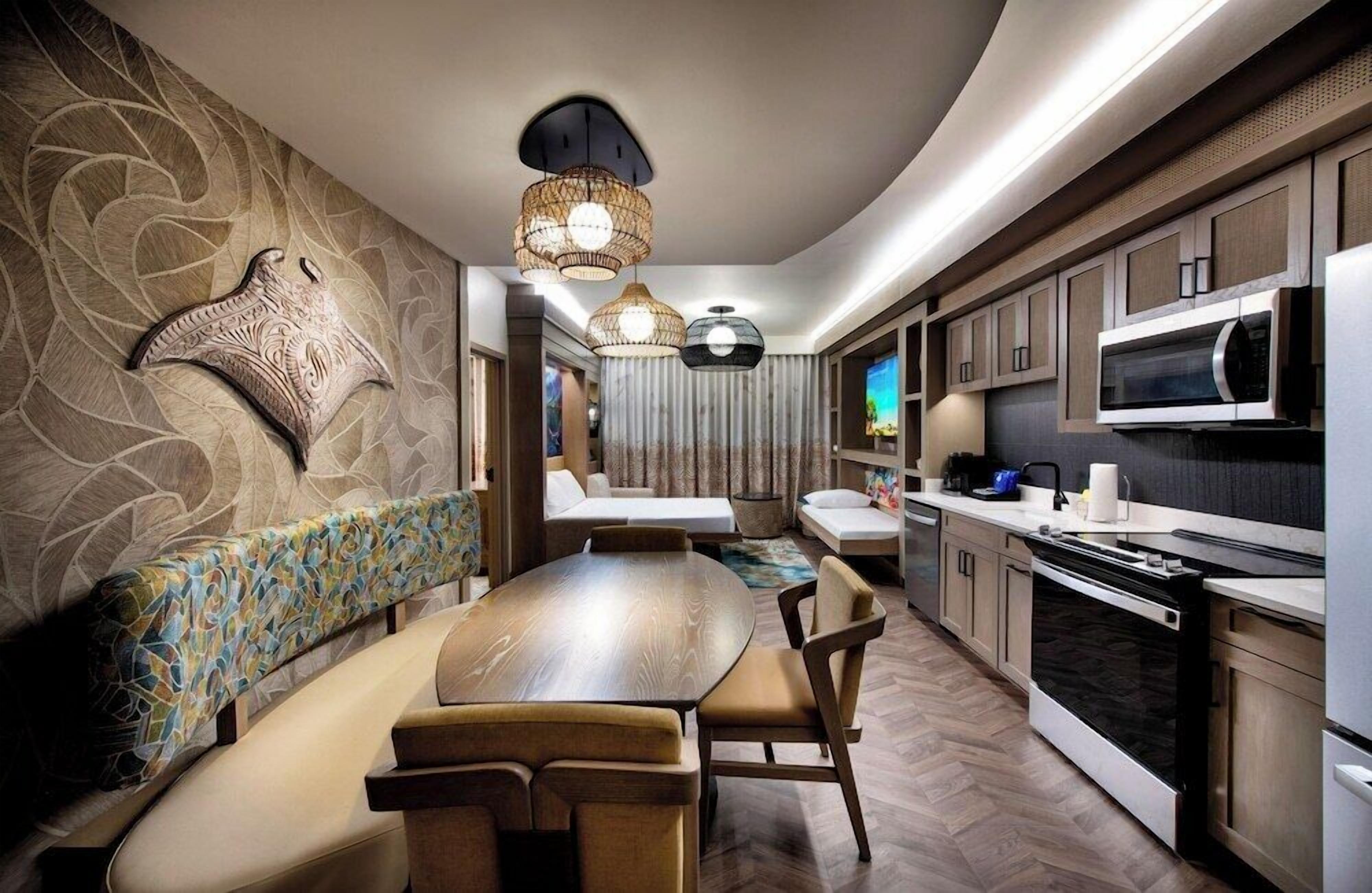 A modern kitchen with a dining area, featuring a large wooden table and chairs, a built-in microwave, and a seating area with a patterned bench.