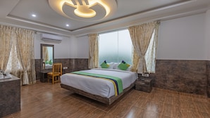 A modern hotel room with a large bed, a wooden chair, a nightstand, and a mirror. - Treebo Siri Ambari Resorts (Piriyapatna)