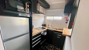 A compact kitchen with a built-in microwave, a sink, and a compact refrigerator. - Apartamento Para Parejas Reformado con Piscina y Wifi (Palafrugell)