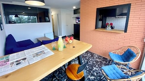 A modern living space with a wooden dining table, blue cushioned seating, a brick accent wall, and a window overlooking a garden. - Apartamento Para Parejas Reformado con Piscina y Wifi (Palafrugell)