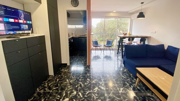A modern living space with a TV, kitchen, dining area, and a balcony. - Apartamento Para Parejas Reformado con Piscina y Wifi (Palafrugell)
