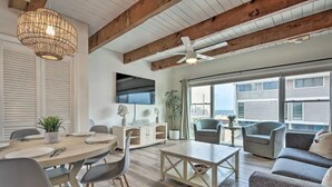 A spacious living room with a wooden ceiling, a dining area with a round table, and a large window offering a view of the outside. - Bethany Townhome-50ft to Shore! (Bethany Beach)