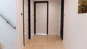 Ein Korridor mit Fliesenboden, einer Tür mit schwarzem Rahmen und einem Gemälde an der Wand.