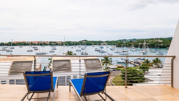 Ein Balkon mit zwei blauen Stühlen und einem Tisch, mit Blick auf einen Hafen voller Boote.