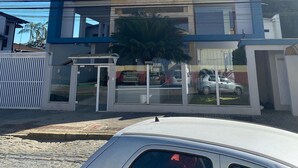 A multi-story building with balconies, a glass entrance, and a car parked in front. - Loft Descolado Glória (Joinville)