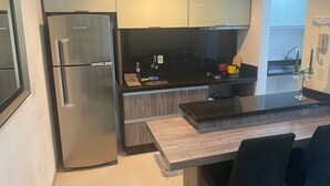 A compact kitchen with a stainless steel refrigerator, a wooden countertop, and a built-in sink. - Loft Descolado Glória (Joinville)