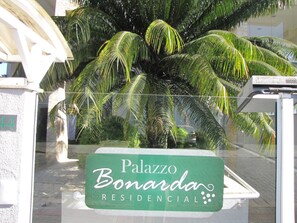 A sign for 'Palazzo Bonarda Residencial' with a large palm tree in the background. - Loft Descolado Glória (Joinville)
