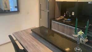 A modern kitchen with a built-in refrigerator, dark countertops, and a small dining area with a chair. - Loft Descolado Glória (Joinville)