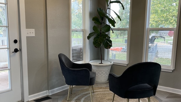 A room with a herringbone wood floor, two dark chairs, a round rug, a potted plant, and a ceiling light fixture. - Modern Home in Gallatin  (Gallatin)
