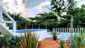 Eine Dachterrasse mit Terrakottafliesen, Pflanzgefäßen, einem weißen Zaun und einem Pool im Hintergrund.