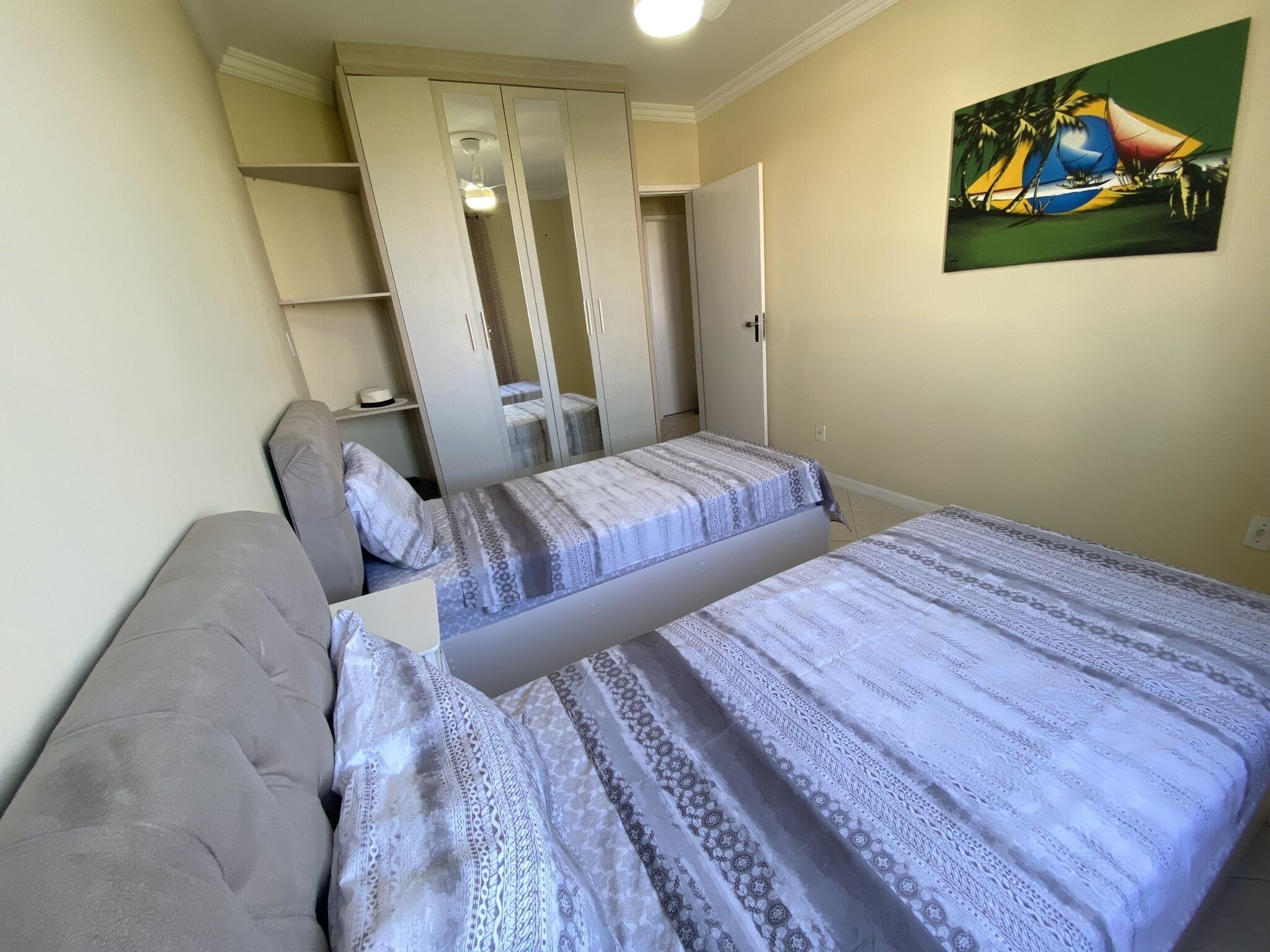 A bedroom with two beds, a wardrobe, and a painting on the wall.