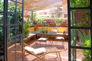Relax in style with a comfortable patio area featuring wicker chairs and a glass table, surrounded by lush potted plants and a stunning city view.