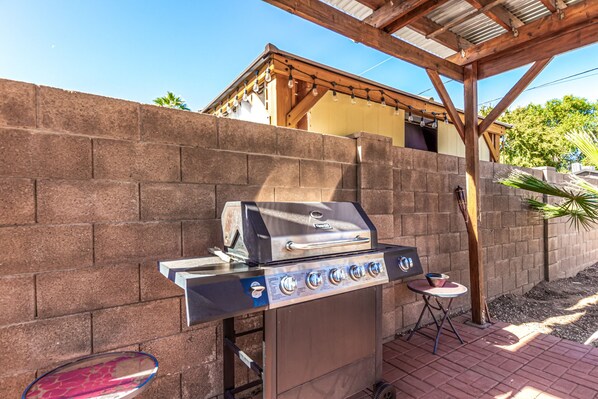 A portable gas grill with four burners, a side table, and a brick wall backdrop.