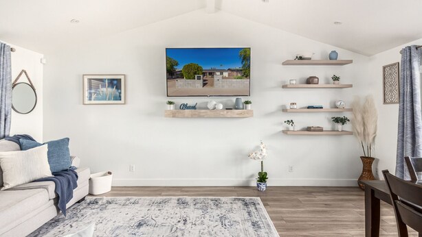 A modern living room with a flat-screen TV mounted on the wall, wooden shelves with decorative items, a comfortable sofa, and a patterned rug. - Serenity in the heart of Phoenix's Camelback East/Biltmore 3 bedrooms 2 baths  (Phoenix)