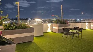 Terraza en la azotea con césped artificial, macetas y una mesa con sillas.